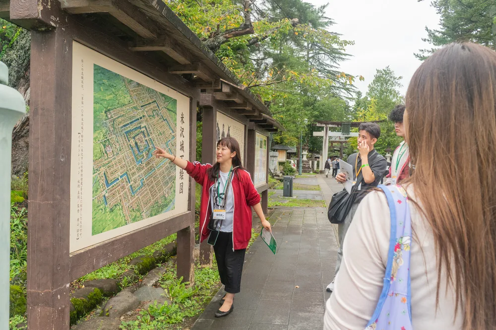 城下町絵図の前で、赤いジャージの校長が学生を案内する