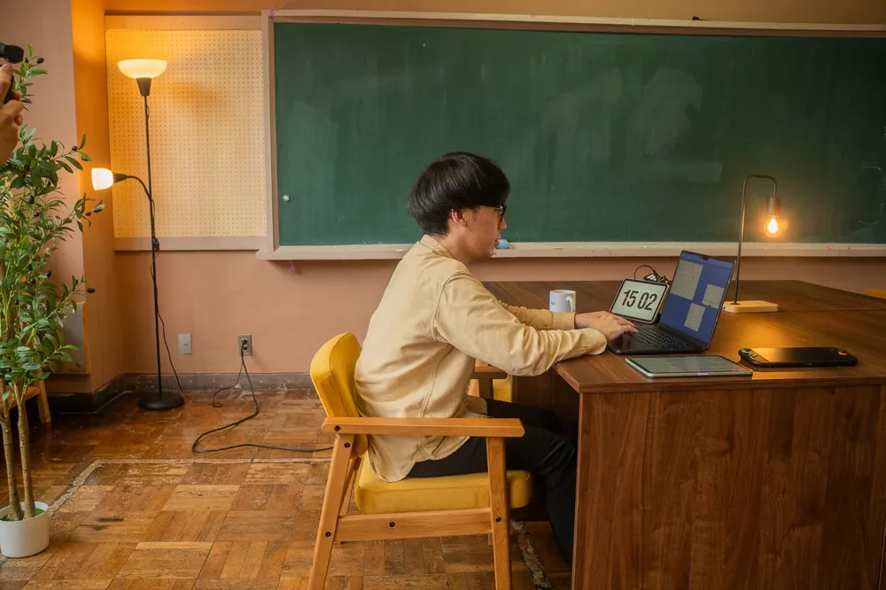 黒板の前の教卓でノートパソコンに向かう人